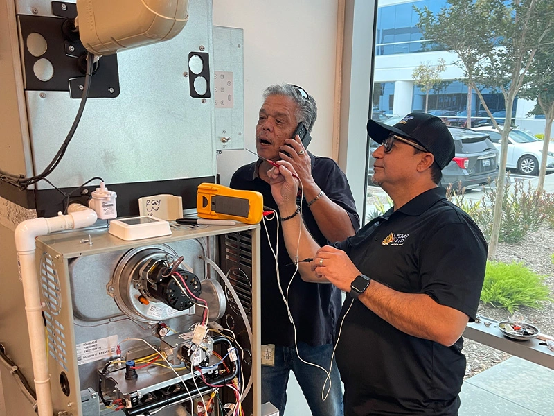 Two technicians working on a furnace system.