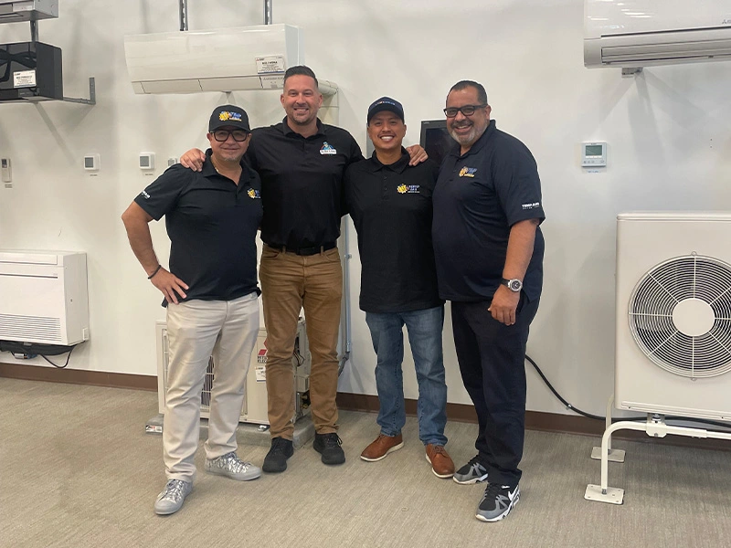Technicians standing in front of various air conditioning units and HVAC equipment.